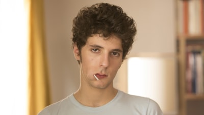 Lolo (Vincent Lacoste) står med en slickepinne i munnen och ser trött och irriterad ut.
