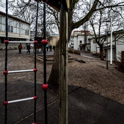Molnig och regnig dag på en lågstadieskolgård. En grupp barn går mot vit matsalsbyggnad.
