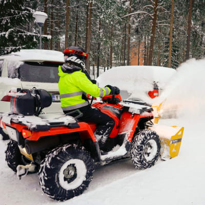 Mönkijän keulaan kiinnitetty lumilinko pöllyttää lunta parkkipaikalla