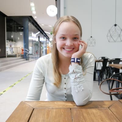 Julia Huovinen sitter vid ett bord, ler och lutar huvudet i handen.