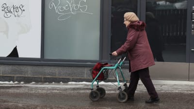 Äldre dam går utomhus med rollator.
