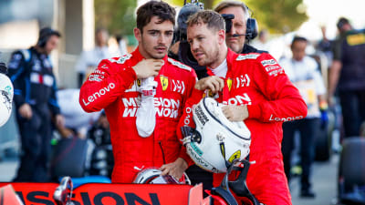 Leclerc och Vettel står bakom en Ferarribil och talar med varandra.