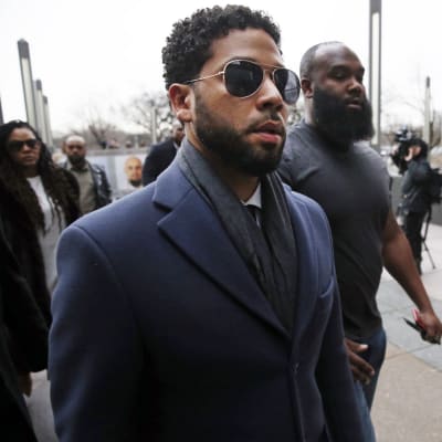Jussie Smollett i solglasögon med storväxt livvakt går förbi pressens kameror.