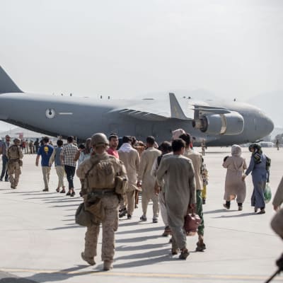 Människor på flygfältet i Kabul går mot en Air Force Boeing C-17 för att evakueras. Soldater går bredvid.