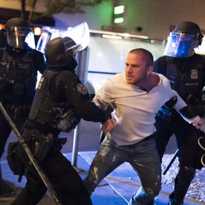 Två poliser håller i en man med vit skjorta som ser ut att kämpa emot.