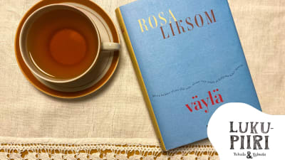 Rosa Liksomin Väylä-kirja ja teekuppi valkoisella pöytäliinalla, kulmassa Lukupiiri Tulusto & Kylmälä -logo.