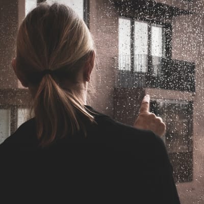 Nainen piirtelee sormellaan sateiseen ikkunaan.