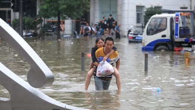 En man bär en kvinna på ryggen genom den översvämmade staden Zhengzhou.