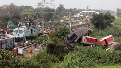 Trasiga järnvägsvagnar ligger bredvid rälsen i Balasore i Indien. Järnvägsarbetare arbetar med rälsen.