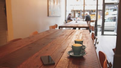 smarttelefon och två tomma koppar på bord i kafé