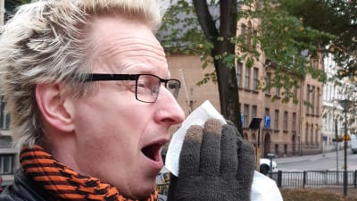 Närbild på Jonas Francks ansikte när han nyser och för en vit näsduk mot ansiktet.
