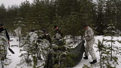 Personer reser ett tält i snöig skog.