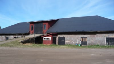 En ladugård i gråsten med stort svart tak. Finns på Rilax gård i Bromarv