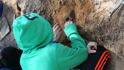 En pojke i grön luvtröja gräver i jorden.