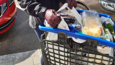 En kundvagn till brädden fylld med livsmedel, kassar och en kvinna som lyfter ut en kasse