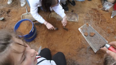 Barn på arkeologiska utgrävningar som håller upp krukskärvor som det hittat.