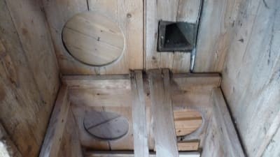 ett gammalt innertak i trä  där man kan se de intäckta gamla hålen från ett utedass.
