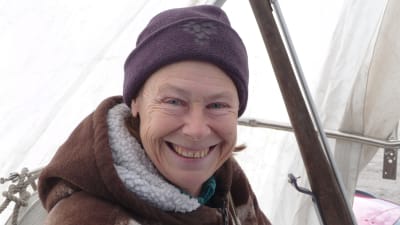 Riitta Airos sitter i sin segelbåt, som ännu är uppe på land och täckt av vit presenning