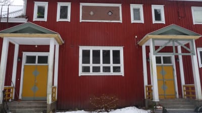 Fasadbild på Vill Christine, en gammal skolbyggnad med rödmyllad brädfodring och senapsgula ytterdörrar.