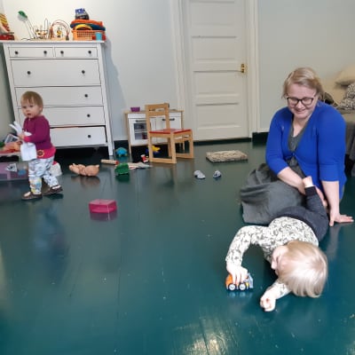 Hanna Räisänen sitter på golvet med två barn som leker med leksaker.