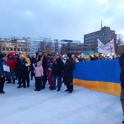 Mielenosoittajia Kokkolan torilla, ihmiset pitävät käsissään suurta Ukrainan lippua.