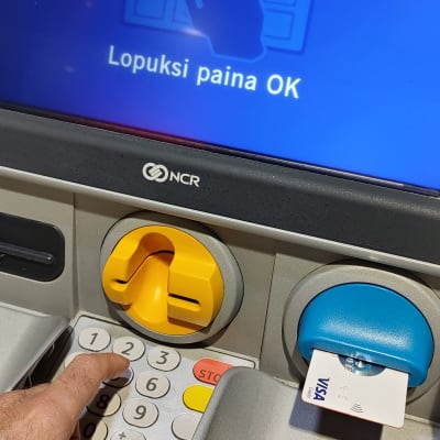 Sormet kirjoittamassa salasanaa pankkiautomaatissa.