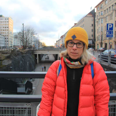 Kvinna i gul mössa och röd jacka står på en bro i centrum av Helsingfors. 