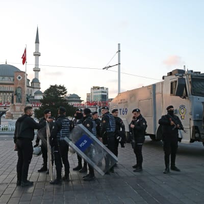 Turkiska poliser med kravallsköldar vid Taksimtorget i Istanbul. I bakgrunden syns turkiska flaggor och en moské.
