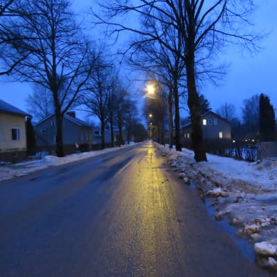En tom, rak gata i Karis. Några gatulampor lyser. Det är tidig morgon, allt går i blått innan solen stiger upp. Vått och grått.