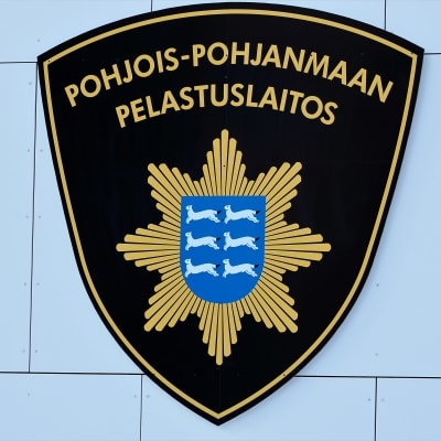 Pohjois-Pohjanmaan pelastuslaitoksen logo paloaseman seinässä.