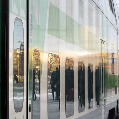 Fjärrtåg vid en perrong, närbild av vagnens fönster som reflekterar passagerare.