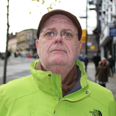 54-åriga Kieran Haunch fotograferad på gågatan i Wigan. Han är iklädd en grann vindjacka och en keps. 