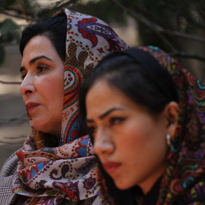 Två afghanska kvinnor i sjalar lutar mot varandra.