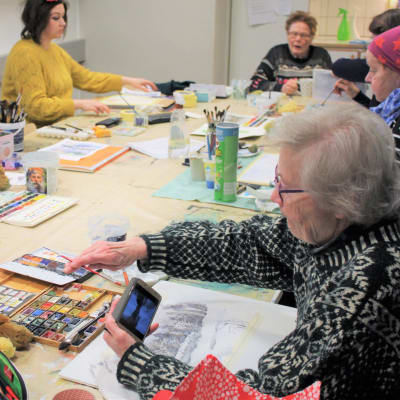 Äldre människor som sitter runt ett bord och målar med akvarell färg.