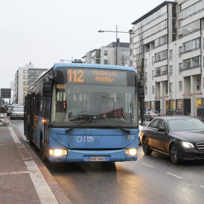 Buss 112 till mattby stannar på hållplats vid biskopsbron i mattby, en våt decemberdag, i bakgrunden höghus