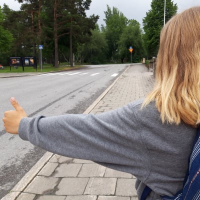 Selin oleva tyttö liftaa kadun reunassa.