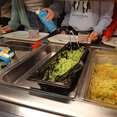 Skolmat i en skolmatsal och elever tar åt sig sallad och mjölk.