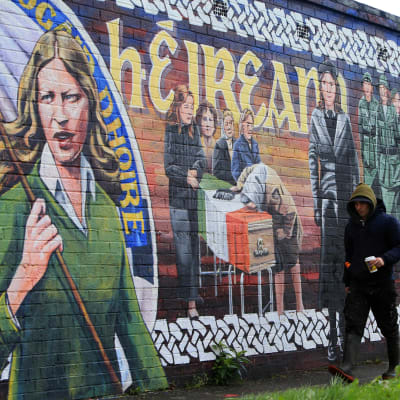 En man går förbi en politisk väggmålning i näheten av Michael McGuinness hem i nordirländska Derry. 