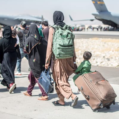 Afghaner på väg att evakueras på flygplatsen i Kabul den 24 augusti 2021. Ett litet barn sitter på en resväska och blickar mot ett av flygplanen.
