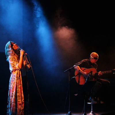 En kvinna iklädd klänning sjunger på en scen.