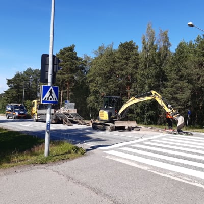 Kaivinkone työstää liikenteenjakajassa paikkaa valopylväälle.