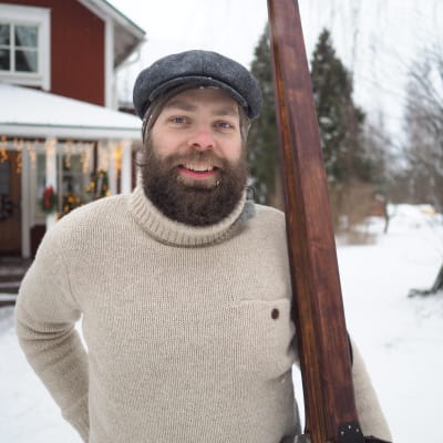 Sipoolainen Lukas Lindberg seisoo kotinsa pihassa pidellen puusuksia ja päällään vanhan ajan tyyliin tehdyt hiihtovaatteet.