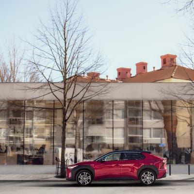 En röd elbil är parkerad framför Åbo stadsbibliotek med sina stora glasfönster.