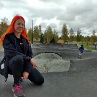 Polvijärven nuorisovaltuuston puheenjohtaja Inka Mustonen kunnan uudella pumptrack-radalla. Taustalla radalla potkulautailevia lapsia.