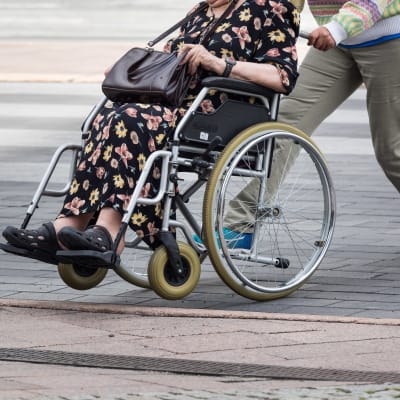 Nainen työntää vanhusta pyörätuolissa.