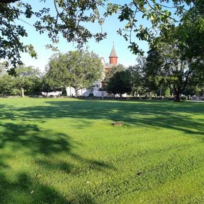 En stor gräsmatta framför Ingå kyrka som heter Kyrkparken.