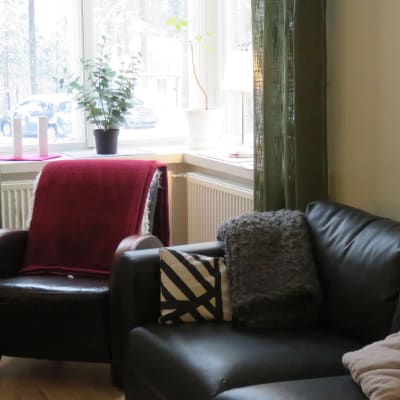 en stol och en soffa i ett hörn av ett rum med fönster i hörnet. Plädar och kuddar gör att det ser trivsamt ut.Ute ser man att det är vinter och snö.