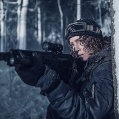 På bilden syns en kvinna som håller i ett gevär i ett vintrigt landskap.