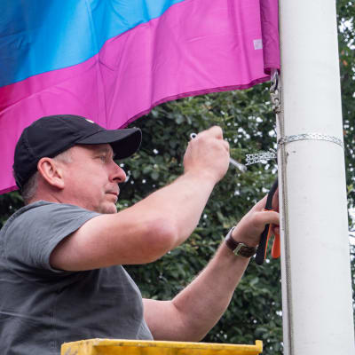 En man spänner fast flagglinan till en regnbågsflagga