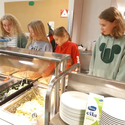 Fyra skolelever tar mat åt sig i skolans matsal.